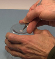 Making a hole in the bottom of the corona motor's jar using an x-acto knife.